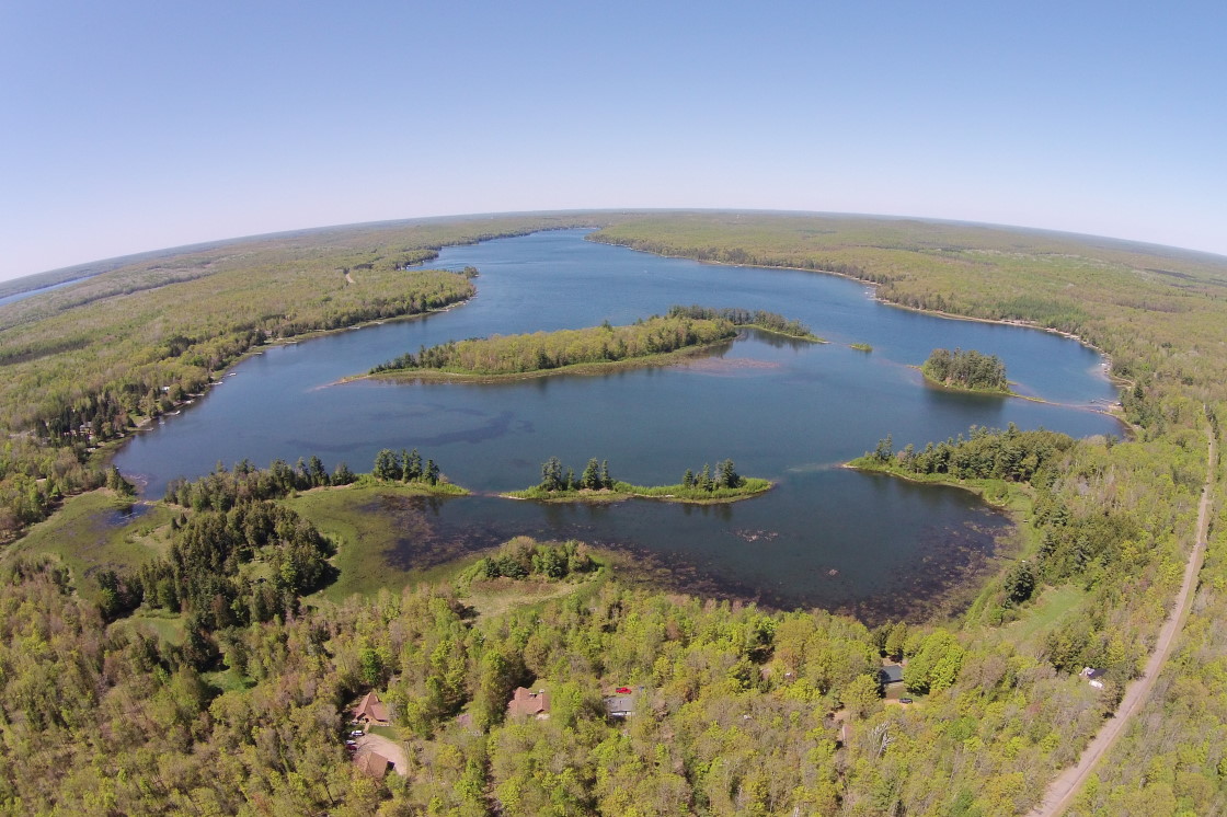 In one of the structures at the LLAA's place, there is a picture of the lake from a plane. Over the years, we've seen reproductions of this image on other walls, curios and even placemats. Since knottlane got the drone it has been our mission to retake that image. Mission Accomplished (<a href='/WeeklySummaryPages/2015/0526/TheBigPictureN.html' class ='defaultlink2' target='_blank'>Full resolution version here</a>).! Yay. The new assignment is to get the same image during the middle of summer, at peak color in Fall, and peak snow in Winter. That, and maybe a top ten list of the cottage signs around the lake. We've always loved the "Skunks -n- Munks" sign, but there are several other really clever and well done placards out there. We'd also like to offer a hardy thank you to the several people we've met as of late and complemented us on one or more of the aspects of this site. As long as folks enjoy knottlane, we will continue to provide updates, contests and other data on beautiful Lake Lucerne, despite the snow and mosquitoes. Both of which we had this week. The snow didn't stick around much. The mosquitoes did, though. Having them on stage at the same time...that was a first.<br><br><br>-Nemo, DEET in one hand, snow shovel in the other.